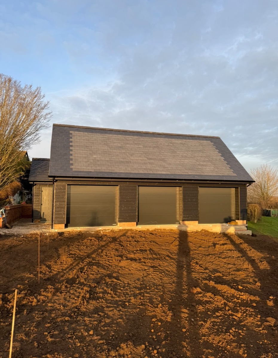 Three bay garage block with dark cladding and solar roof tiles