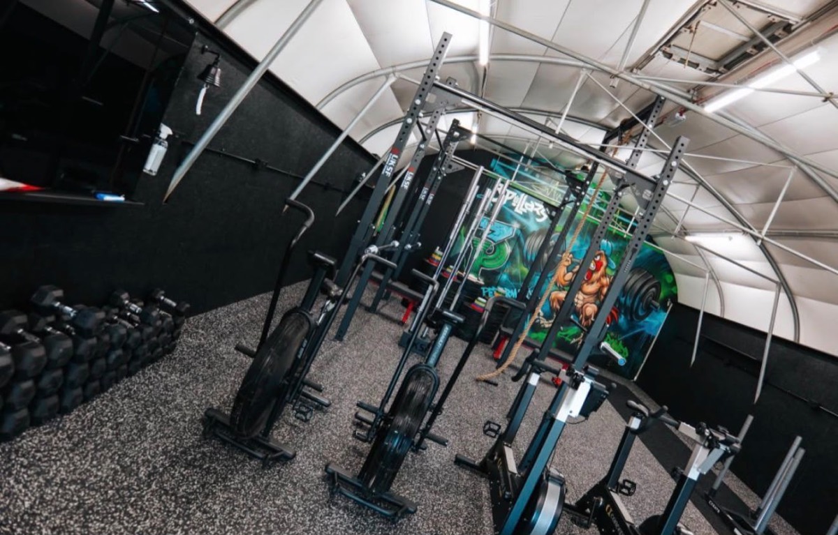 Wide view of the gym with racks, air bikes and rear mural